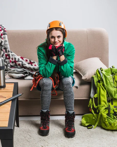 Schöner Bergsteiger im Helm mit Rucksack und Kletterausrüstung auf Sofa sitzend — Stockfoto