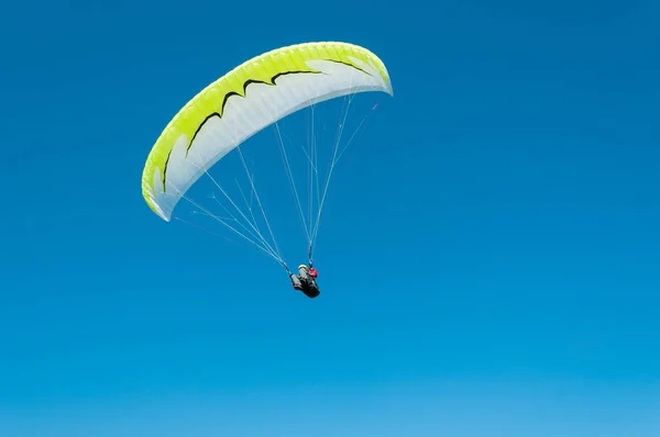 Mavi gökyüzünde uçan yamaç paraşütü pilotu. Alt görünümü