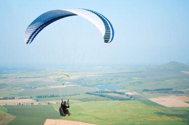 Arka plan mavi gökyüzü ve dağ alanların üzerinde bir yamaç üzerinde uçan sporcu