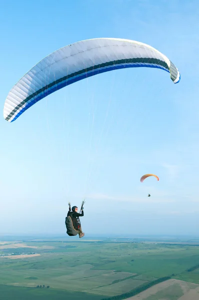 Arka plan mavi gökyüzü ve diğer sporcu alanların üzerinde bir Yamaçparaşütü üzerinde uçan sporcu