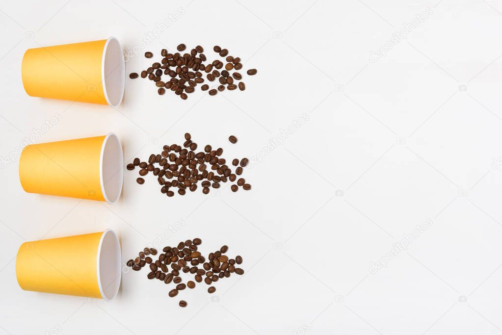 Yellow paper cups and splashes of coffee beans. White and grey textural background. Coffe to go concept. Flatlay.