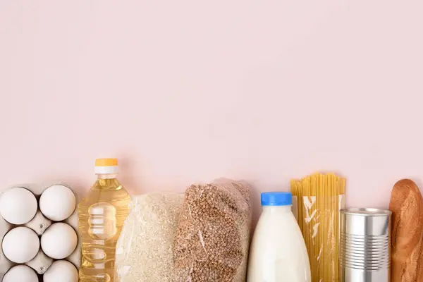 Güvenli yemek teslimatı. Pirinç, teneke kutu, karabuğday, ayçiçeği yağı, açık pembe arka planda spagetti ve baget. Coronavirus temel gıda seti. Üst Manzara. Uzayı yukarıdan kopyala.