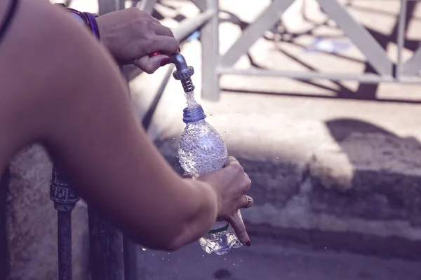 girl pours water into a bottle from street fountain with clean d