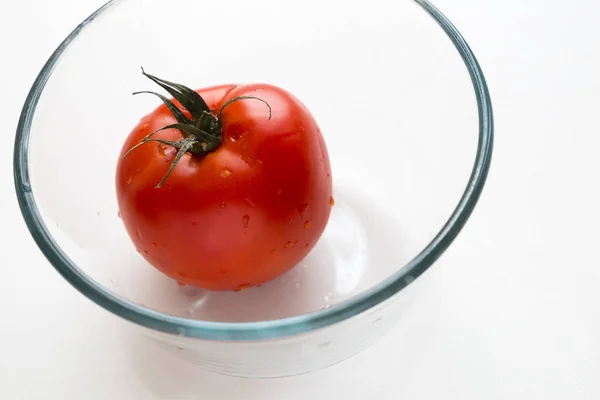 Juicy appetizing tomato with water drops in glass cup on the white background — Stock Photo, Image