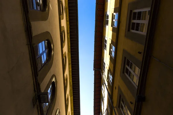 Cielo azul se ve a través de los techos de las casas en una calle estrecha al atardecer —  Fotos de Stock