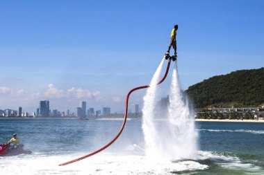adam sahilde deniz mavi gökyüzü, şehir ve dağ ile arka planda bir flyboard biniyor