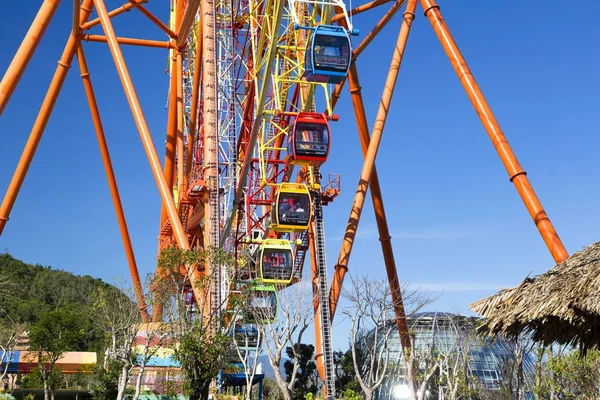 Edificios asiáticos tradicionales sobre un fondo de una enorme rueda de ferris brillante colorido moderno en un parque de atracciones sobre un fondo de cielo azul —  Fotos de Stock