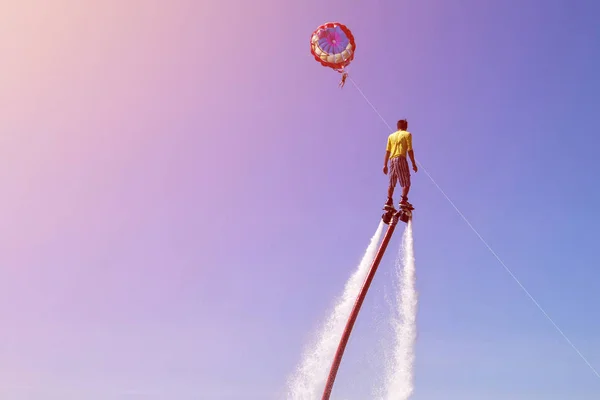 Hombre está montando un flyboard en la playa del mar con cielo azul y paracaídas en el fondo —  Fotos de Stock
