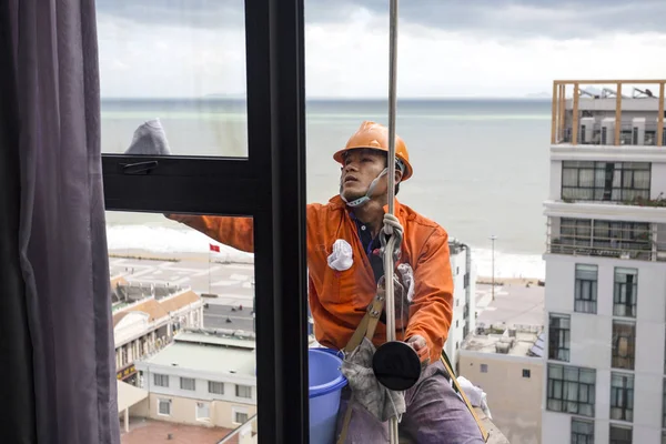 Limpiador de ventanas escalador industrial en uniforme naranja y casco en el trabajo con el mar en el fondo Vietnam, Nha Trang 2018-01-1 — Foto de Stock