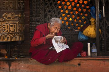KATMANDU, NEPAL - CIRKA NOVEMBER, 2017: Tapınağın önünde yemek yiyen yaşlı Budist keşiş