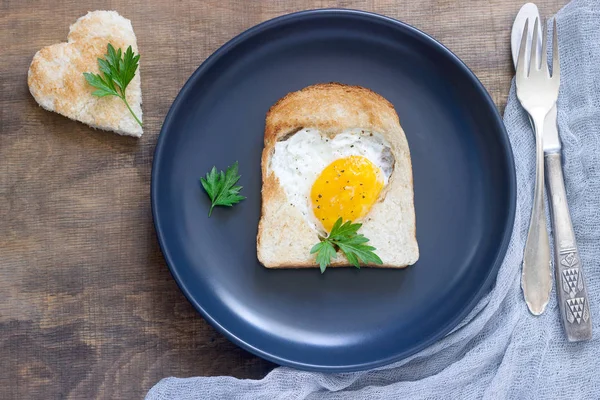 Egg in a heart-shaped bread with parsley, romantic breakfast. — Stock Photo, Image