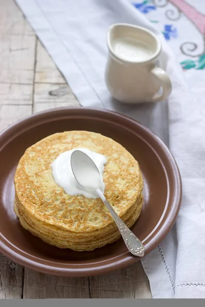 Pilha de panquecas russas com nata azeda - blini em uma chapa na mesa de madeira . — Fotografia de Stock