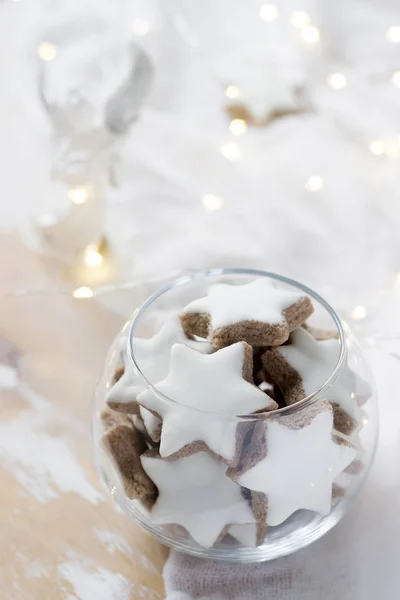 Cookies kaneel ster in een glasvaas op een witte achtergrond versierd met een beeldje van een engel en een slinger. — Stockfoto