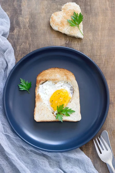 Egg in a heart-shaped bread with parsley, romantic breakfast. — Stock Photo, Image