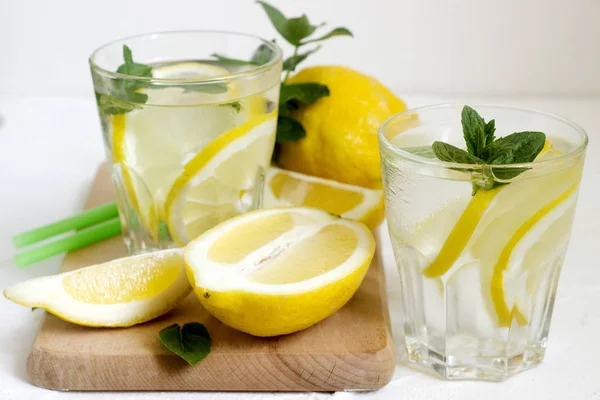 Limonade mit Zitronenscheiben, Minze und Eis und Zitronen auf hellem Betongrund. rustikaler Stil. — Stockfoto