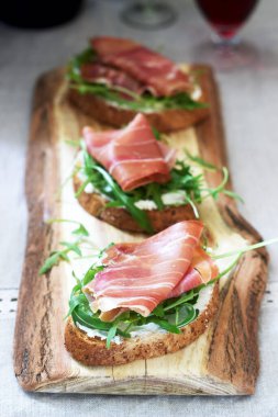 Traditional italian appetizer bruschetta of toasted bread with cottage cheese, arugula and prosciutto.