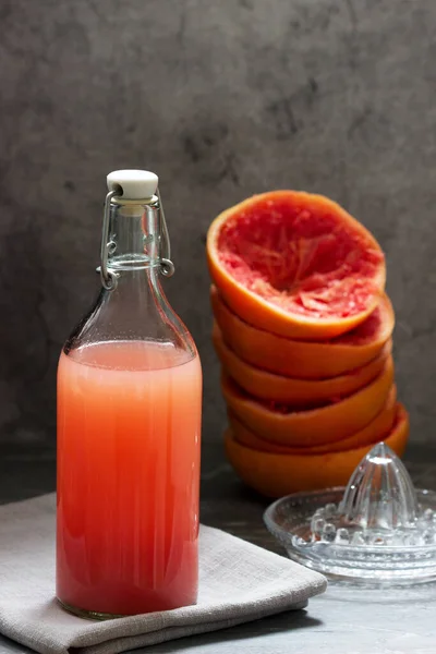 Свежевыжатый грейпфрутовый сок в стеклянной бутылке, соковыжималка и фруктовая кожура на бетонном фоне . — стоковое фото