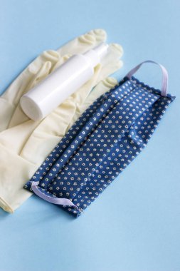 Kişisel koruyucu ekipman maskesi, eldivenler ve mavi arka planda dezenfektan. Seçici odak.