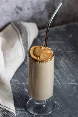 Dalgona Kahvesi şeffaf bir fincanda beton bir masada kokteyl pipetiyle. Seçici odak.