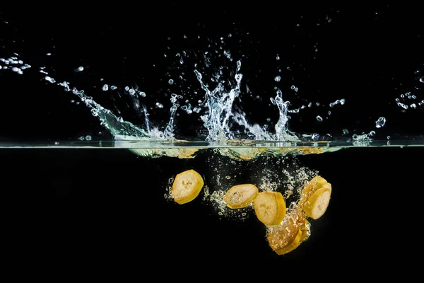 Pezzi di banana che cadono in acqua con spruzzi — Foto Stock