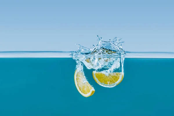 Fette di limone che cadono in acqua con spruzzi — Foto Stock