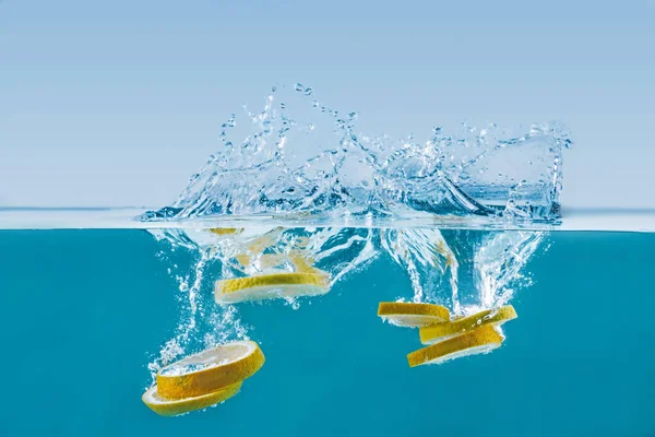 Lemon slices falling into water with splashes — Stock Photo, Image