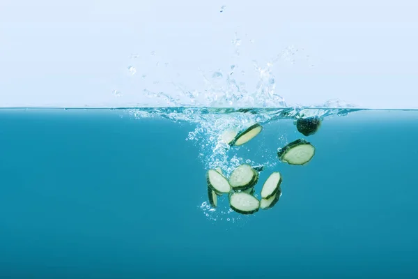 Plakjes komkommer vallen in water met spatten — Stockfoto