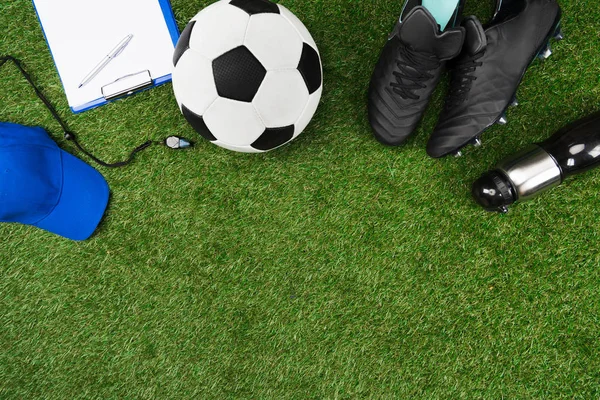 Prancheta com bola de futebol e botas na grama — Fotografia de Stock