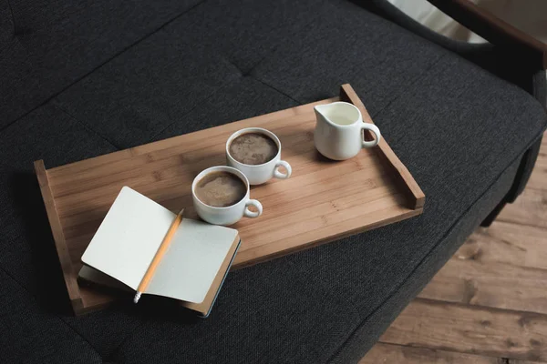 Coffee, jug of milk and notebook on tray — Stock Photo, Image