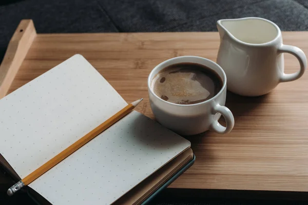 Kaffe, kanna med mjölk och anteckningsboken på bricka — Stockfoto