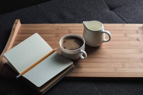 coffee, jug of milk and notebook on tray