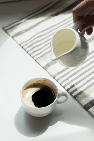 Pouring milk into cup of black coffee — Stock Photo, Image