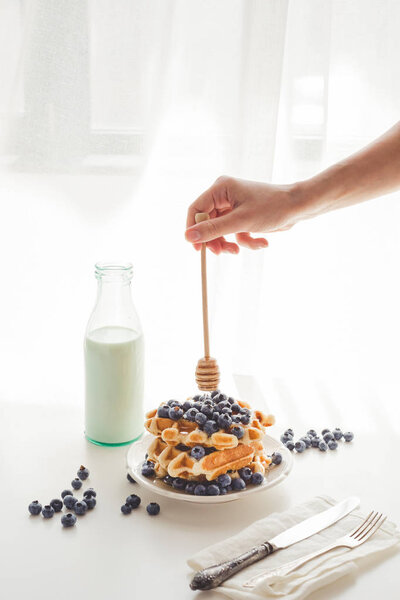 woman pouring honey on tasty waffles