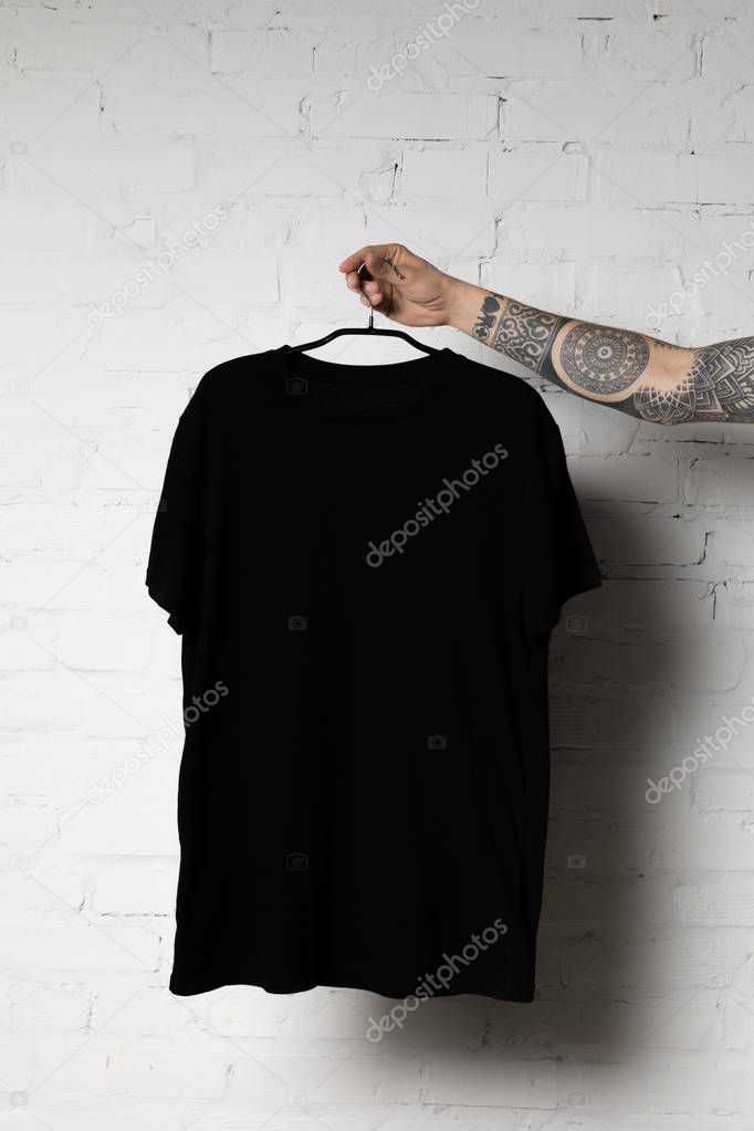 Cropped shot of man holding hanger with blank black t-shirt