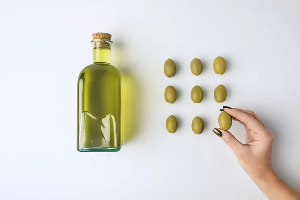 Botella de aceite y mujer sosteniendo oliva — Foto de Stock