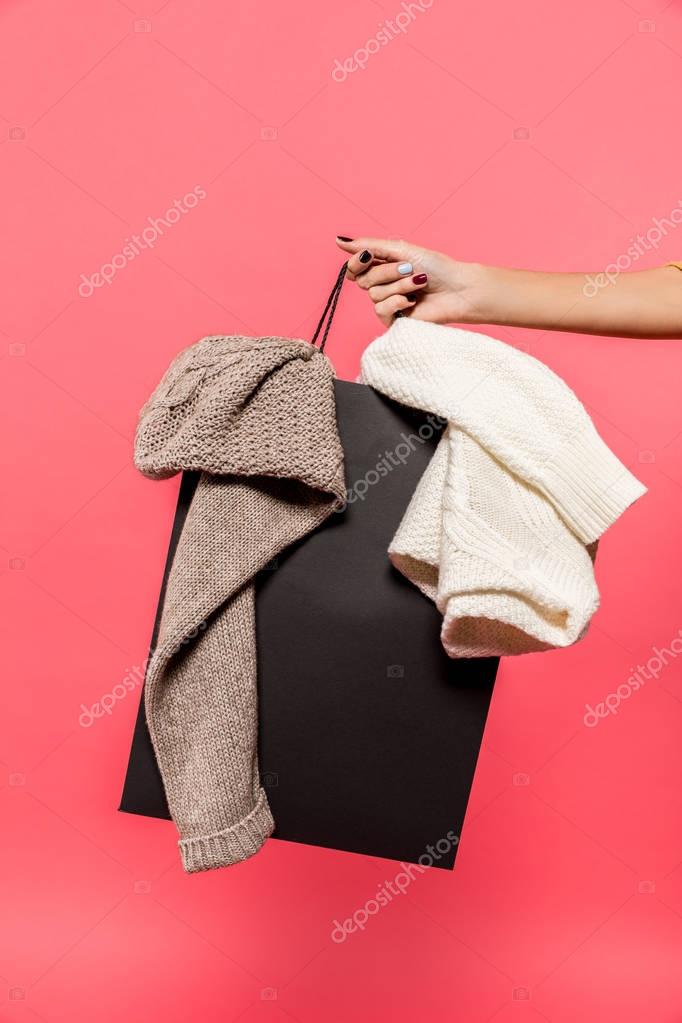 Cropped shot of woman holding black shopping bag with clothes isolated on white