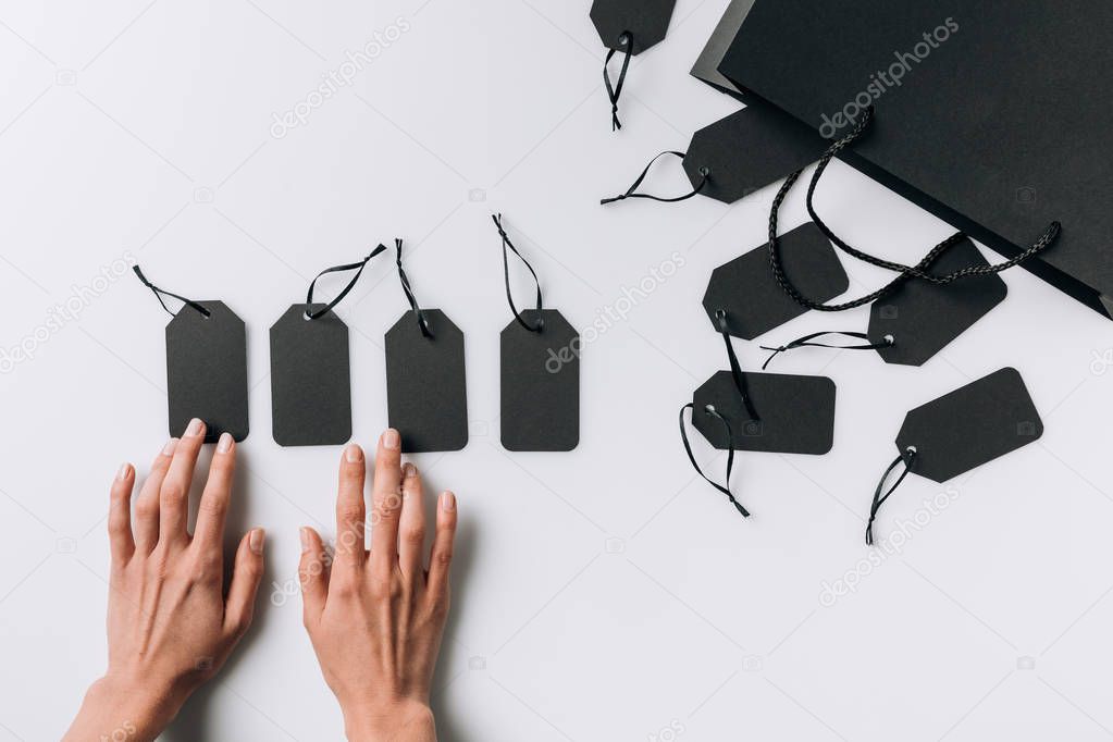 Partial view of female hands, black blank labels and shopping bag isolated on white