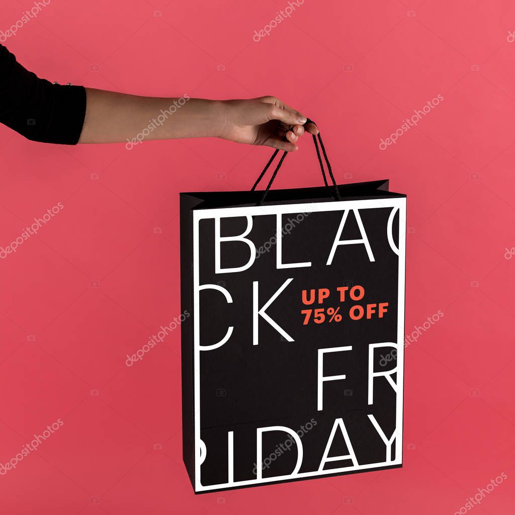 Cropped shot of woman holding black shopping bag isolated on red