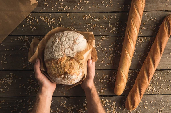 Loaf of bread in hands and baguettes — Stock Photo, Image