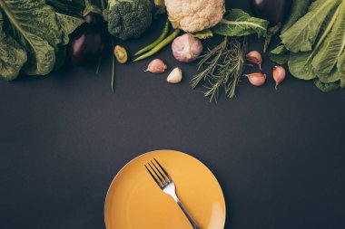 top view of fork on plate and vegetables on gray table clipart
