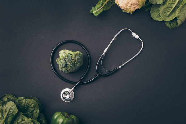 top view of stethoscope with broccoli and cauliflower on gray table 