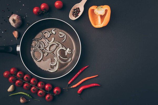 top view of frying pan with onion and oil among vegetables on gray table 