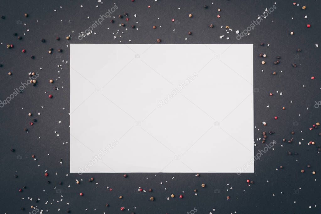 top view of white sheet of paper among scattered pepper on gray table