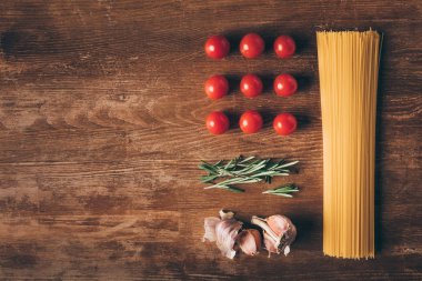 flat lay with row pasta, tomatoes, rosemary and garlic on wooden table clipart