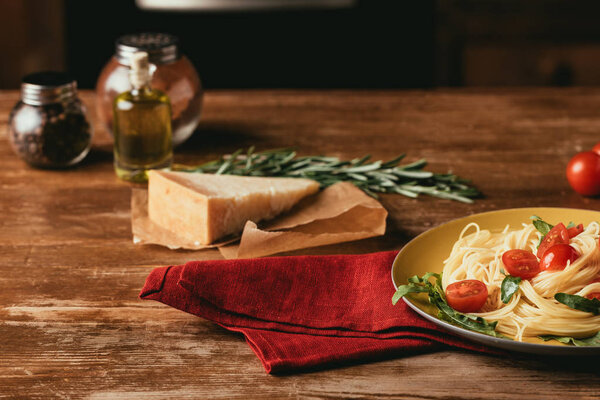 traditional italian pasta with tomatoes and arugula in plate on wooden table with Parmesan, rosemary and oil