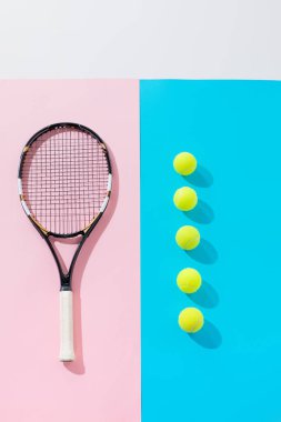 top view of tennis racket on pink and yellow balls in row on blue  clipart