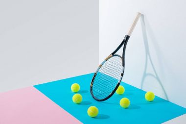 yellow tennis balls on blue and pink papers and tennis racket at white wall