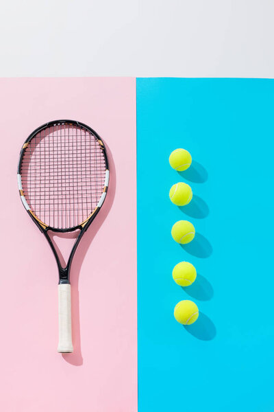 top view of tennis racket on pink and yellow balls in row on blue 