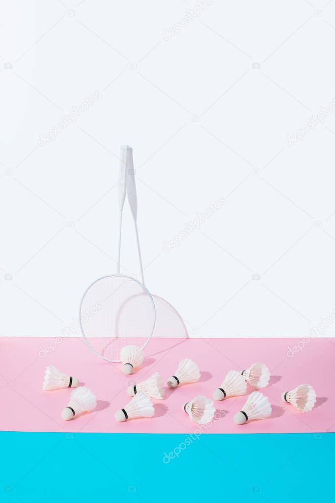 badminton racket and shuttlecocks on blue and pink papers at wall