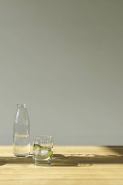 bottle with mineral water and glass with water and cucumber on wooden table clipart
